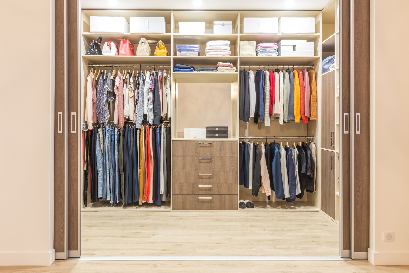 Modern wooden wardrobe with clothes hanging on rail in walk in closet